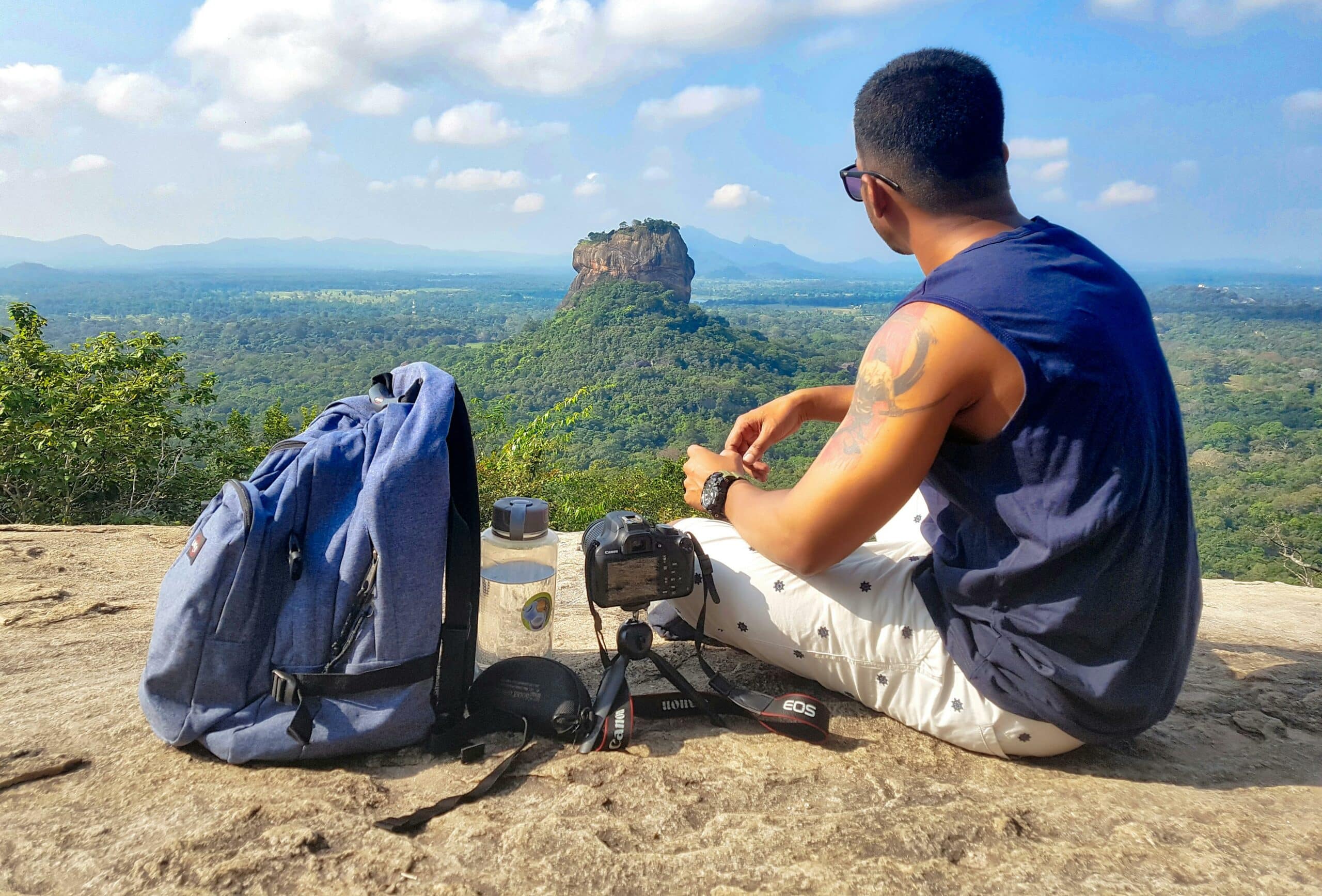 Mann, Der Oben Auf Grauem Klippen Berg Neben Rucksack, Wasserflasche Und Kamera Sitzt